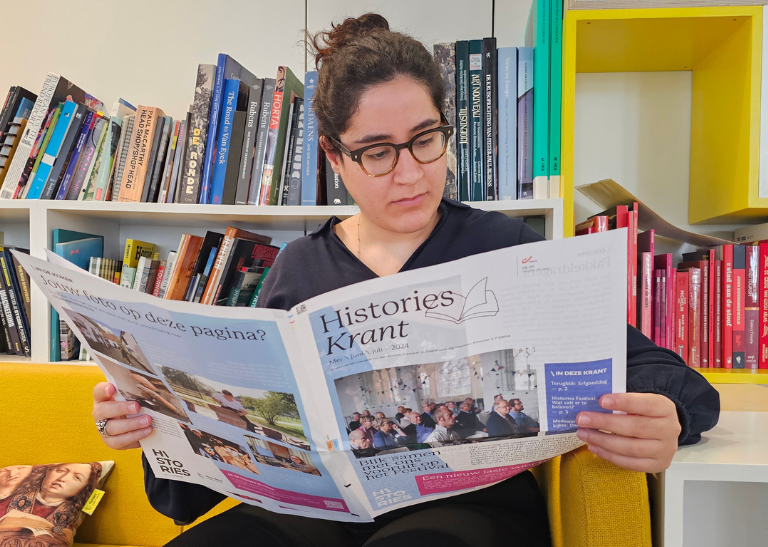 Een jonge vrouw met een bril en zwart haar leest de laatste editie van de Histories Krant