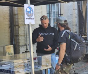 Een metaaldetectorist legt iets uit aan een nieuwsgierige voorbijganger