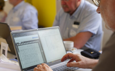 Close-up van handen op een laptop tijdens een werksessie met digitale historische documenten.