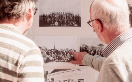 Twee oudere mannen bekijken oude zwart-witfoto's op een muur