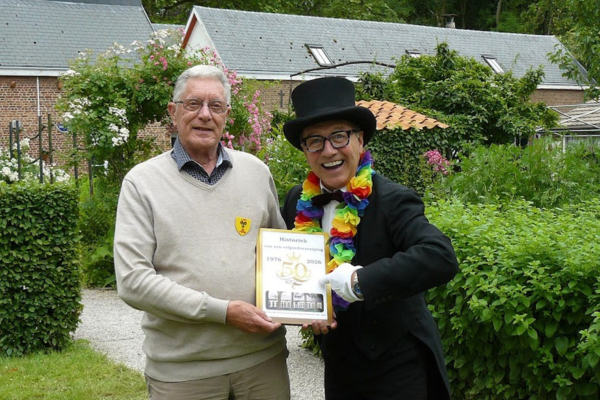 Een man in zwart kostuum en zwarte hoed poseert naast een lid van Heemkundige kring Eugeen Goeyvaerts vzw Lint. Ze houden een boek vast.