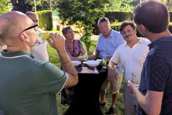 Een groep staat rond een zwarte tafel. Ze drinken en babbelen.