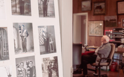 Een man zit op de achtergrond. Op de voorgrond zie je een tentoonstelling met oude foto's.