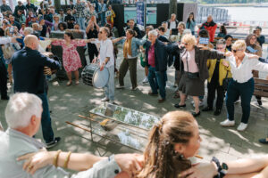 Mensen dansen op straar met in het midden een man die de Bouzouki bespeelt