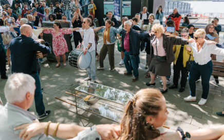 Mensen dansen op straar met in het midden een man die de Bouzouki bespeelt