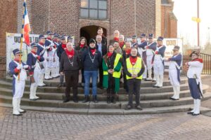 Groep mensen op de trappen van een kerk die geflankeerd worden door muzikanten in uniform