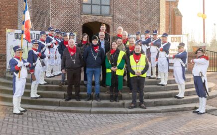Groep mensen op de trappen van een kerk die geflankeerd worden door muzikanten in uniform