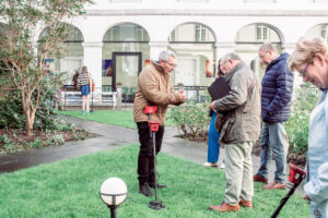 Een man geeft uitleg aan een groep mensen die een metaaldetector uitproberen