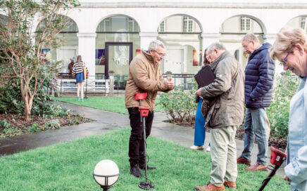 Een man geeft uitleg aan een groep mensen die een metaaldetector uitproberen