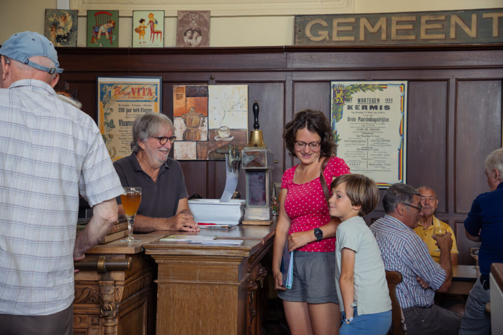 Moeder en zoon staan aan de bar die wordt bediend door een man met bril en baard