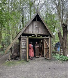 Twee vrouwelijke vrijwilligers van de Gallische Hoeve staan in de deuropening van een huisje in het bos